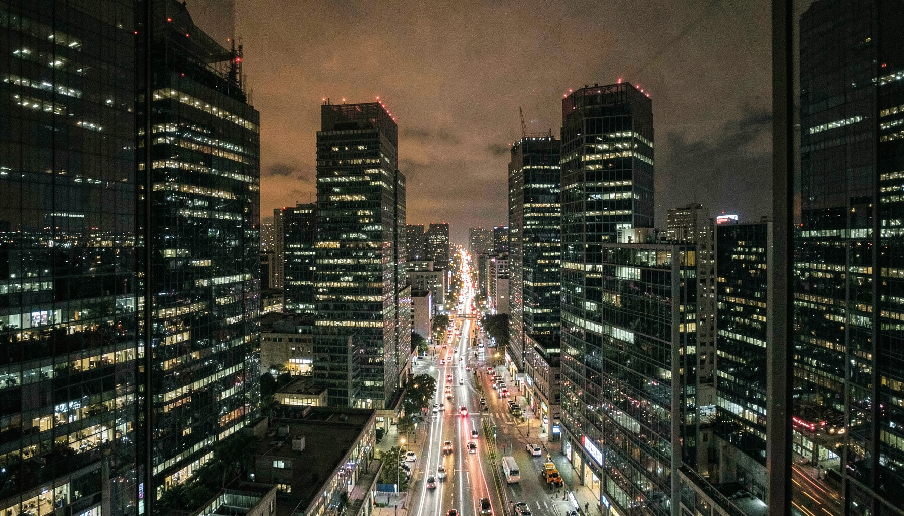 Distrito financiero de noche con torres de oficinas iluminadas y tráfico en la avenida, ilustración del artículo sobre malware en cajeros automáticos