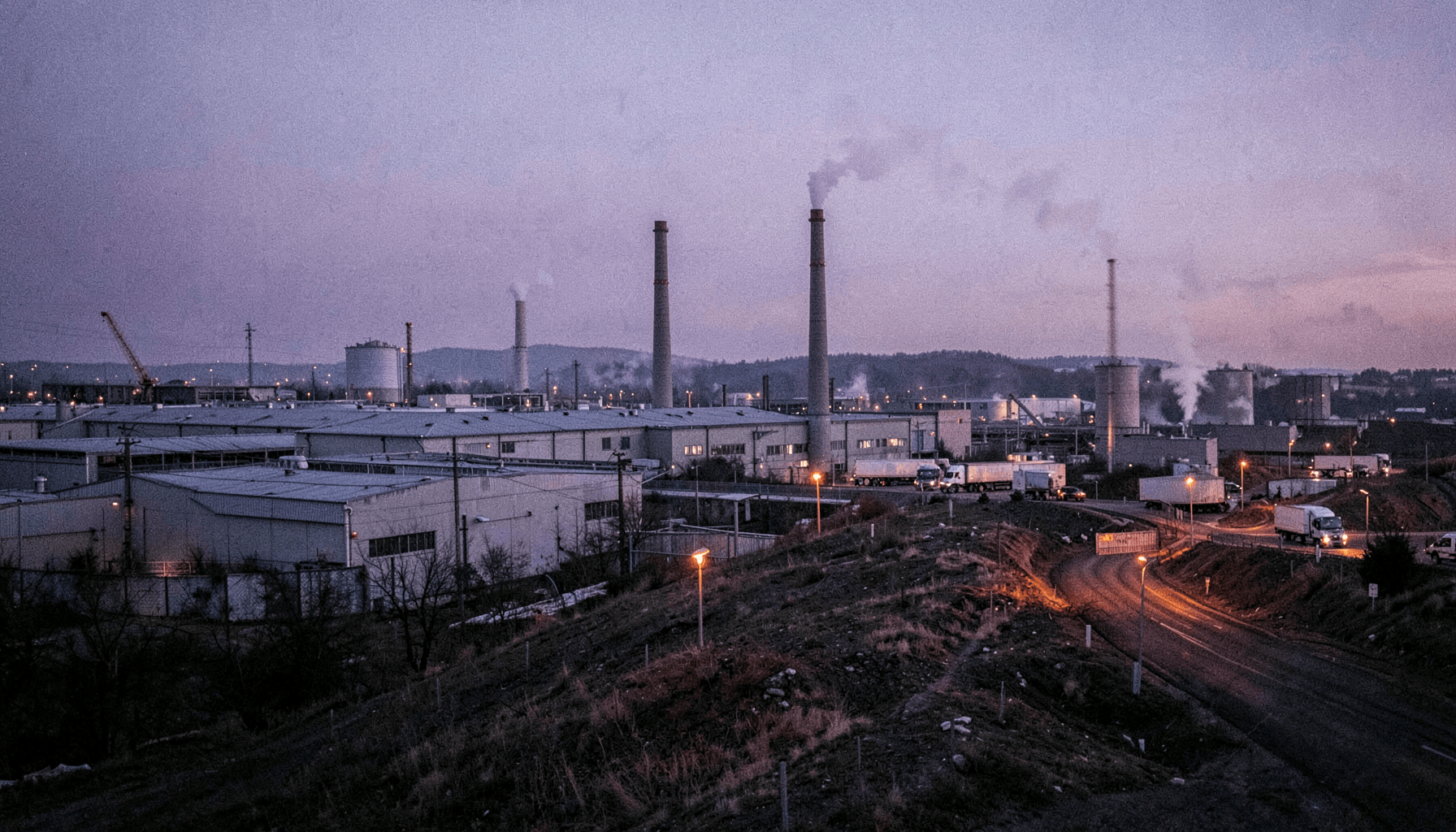 Parque industrial al anochecer con chimeneas, tanques y camiones esperando en la entrada, sobre monitoreo de comunicaciones internas